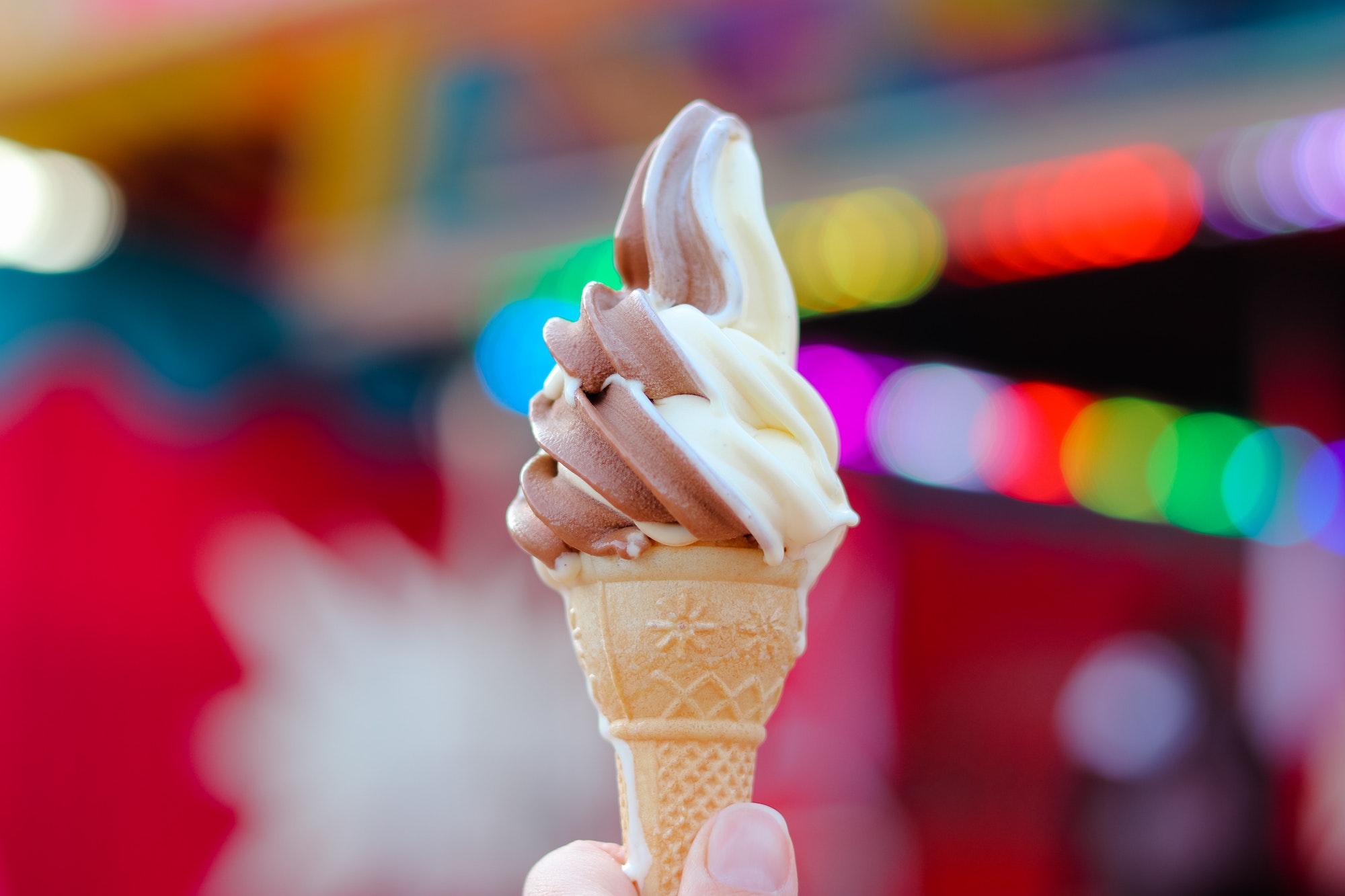 Hand holding chocolate and vanilla soft ice cream in waffle cone with blurred bright colorful